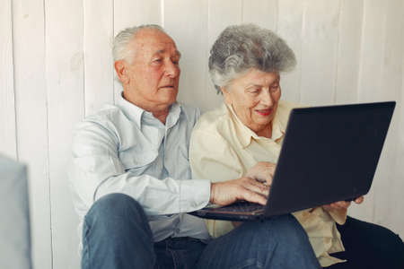 Elegant old couple sitting at home and using a laptopの写真素材