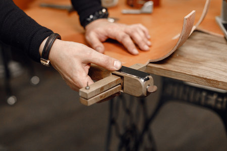 Cropped photo of a leather craftsman hands working on a belt