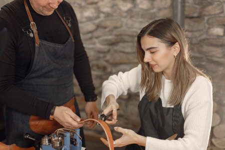 Leather craftsman with masters apprentice working on a beltの写真素材
