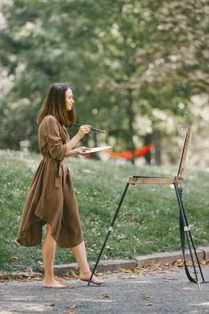 Girl in dress painting on an easel in a park barefootの写真素材
