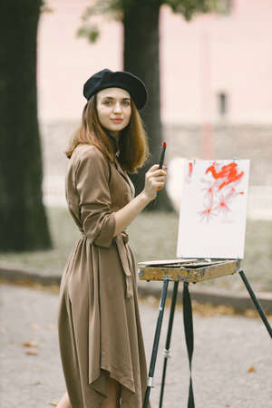 Girl in dress and black hat painting on an easel in a parkの写真素材