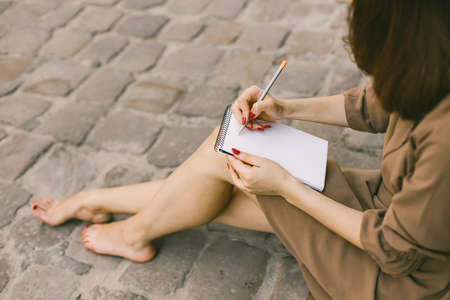 Cropped photo of a woman in dress with a pensil writing in a notebookの写真素材