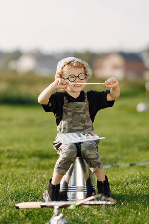 Blonde curly boy sitting on a bucket and holding a box with a baits for fish