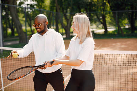 Black man teaching young woman to play tennisの写真素材