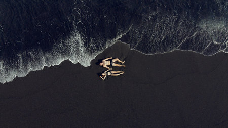 Couple lie on a black sand near ocean