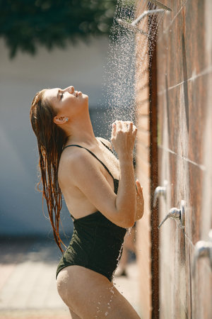 Caucasian woman posing in a swimwear under a shower outdoors
