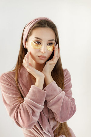 Portrait of brunette woman in rose pajamas applying a face patchesの写真素材