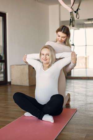 Trainer helping pregnant woman to do yoga asanaの写真素材