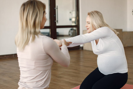 Trainer helping pregnant woman to do yoga asana