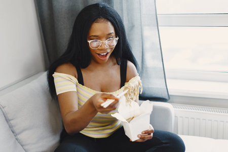Beautiful young african american woman eating noodles