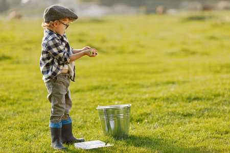 Blonde curly boy standing on a grass and holding a box with a baits for fish