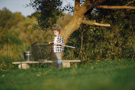 Blonde curly boy standing on a grass and holding a fishing rodの写真素材