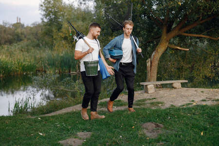 Two men walking and carrying fishing equipment outdoorsの写真素材