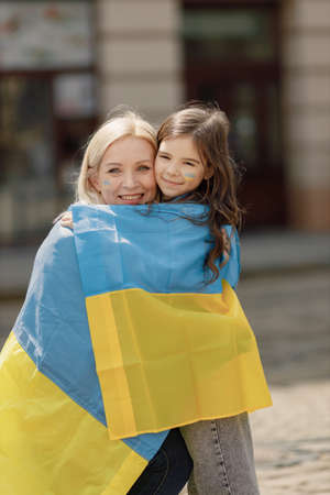 Mother and her daughter hugging with a flag of Ukraine on a streetの写真素材