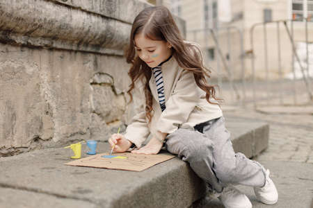 Little girl with a flag of Ukraine on a cheek draw a poster supporting Ukraineの写真素材