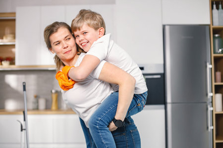 Little boy and his mother cleaning in a kitchen wearing rubber gloves
