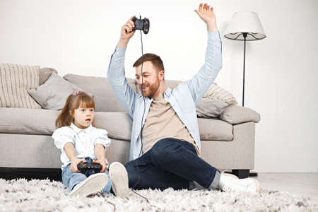 Girl with Down syndrome and her father sitting on a floor and playing PlayStationの写真素材
