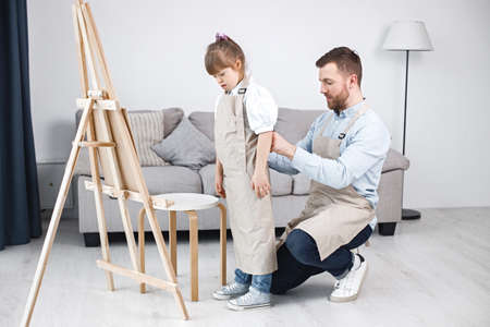 Father helping his daughter with Down syndrome to wear an apronの写真素材
