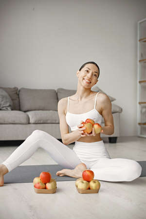 Young fitness woman sitting on yoga mat at home and holding fresh applesの写真素材