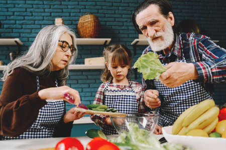 Senior grandparents couple with dgranddaughter cooking in kitchenの写真素材