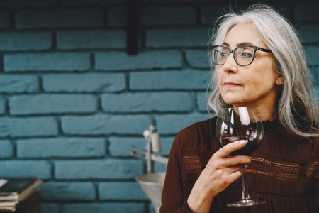 Portrait of beautiful happy senior woman with glass of red wine at home