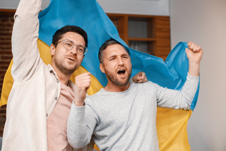 Two men watching a football game on tv and holding big flag of Ukraineの写真素材