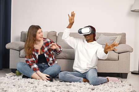 Two young teenage girls sitting on a floor near bed wearing a virtual reality glassesの写真素材