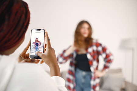 Black girl take a photo of her caucasian girlfriend while standing at home