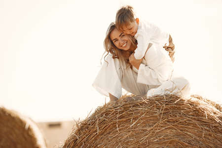 Mom and son are sitting on a haystack in the field at sunsetの写真素材