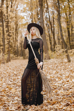 Young witch in forest on Halloween with a broom