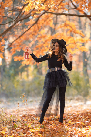 Woman in witch costume standing in autumn forest on Halloween