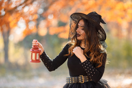 Woman in witch costume standing in autumn forest on Halloween