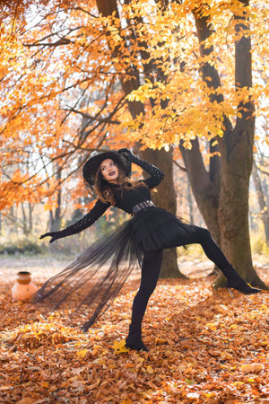 Woman in witch costume standing in autumn forest on Halloween