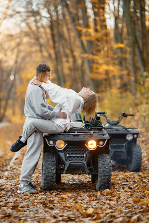 Man and woman hugging on a quad bike in autumn forestの写真素材