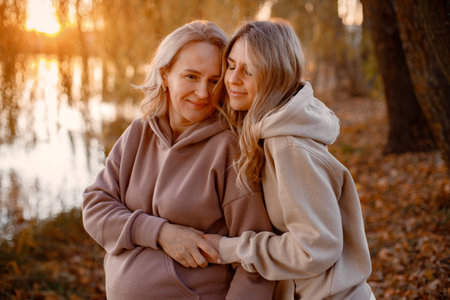 Adult daughter hugs her pregnant mom while standing in autumn park