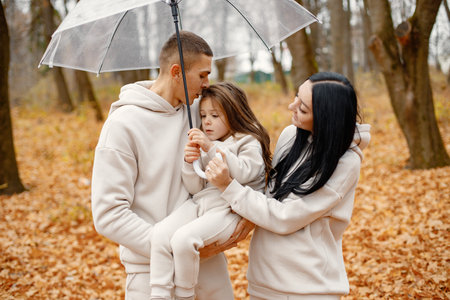 Young family standing in autumn forest under transparent umbrellaの写真素材