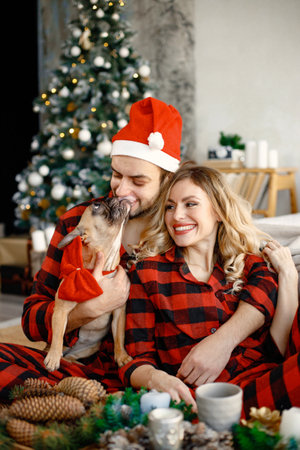 Couple wearing christmas plaid red pajamas sitting on the floor with a dogの写真素材