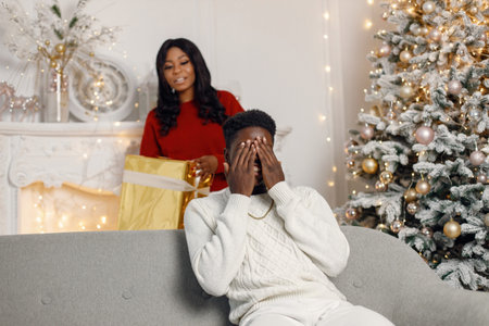 Young black woman make a surprise for her boyfriend in Christmas eveの写真素材