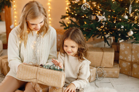 Little girl and her mom sitting near Christmas tree with gift boxの写真素材