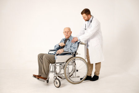 Male doctor and old man on a wheelchair isolated on a white backgroundの写真素材