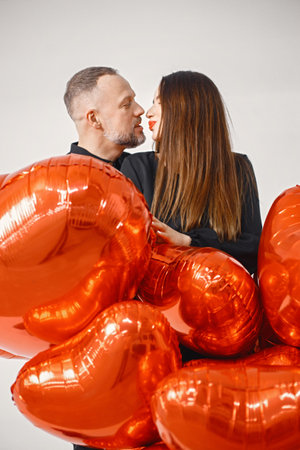 Man and woman holding bunch of heart-shaped red ballons and posing in studioの写真素材