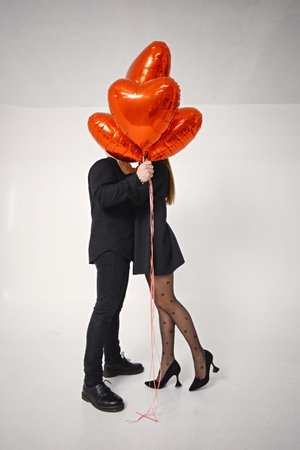 Man and woman kissing covering with bunch of heart-shaped red ballons