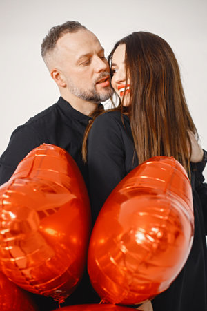 Man and woman holding bunch of heart-shaped red ballons and posing in studioの写真素材