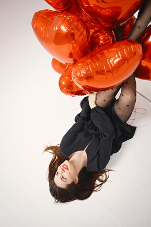 Brunette woman holding a bunch of heart-shaped red balloons in studioの写真素材