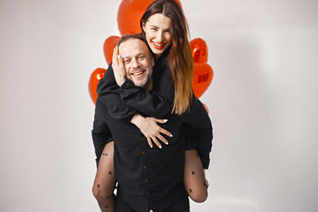 an carrying woman piggyback while posing in studio near bunch of heart-shaped ballons