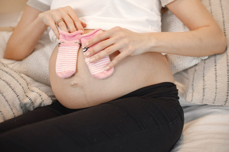 Midsection of pregnant lady lie on a bed and holding a little baby socks