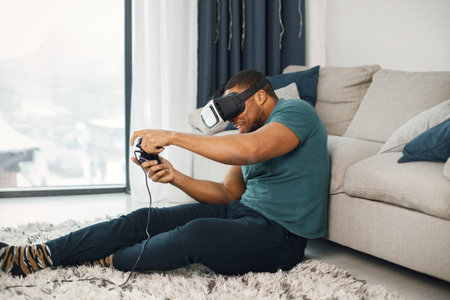 Black guy with virtual reality glasses sitting on a carpet in living room