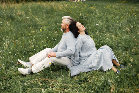 Senior couple sitting on a grass in a park back to backの写真素材