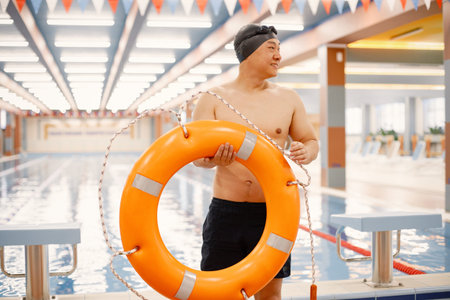 Asian man standing in indoors swimming pool and holding a swimming circleの写真素材