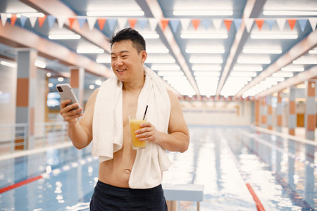 Asian man standing in indoors swimming pool and using a phone